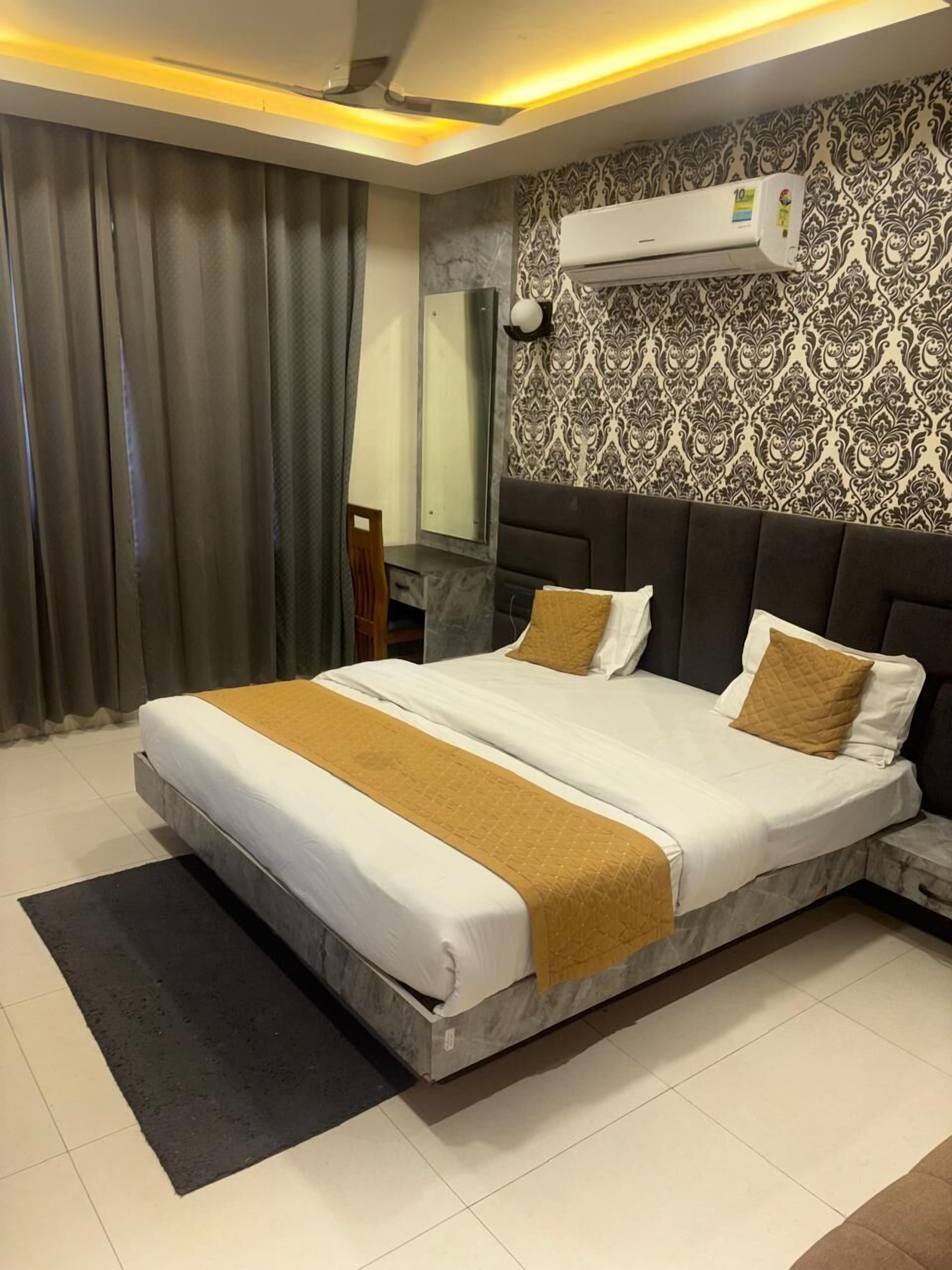 A modern hotel room with a large bed, a desk, a chair, an air conditioning unit, and a patterned wall.