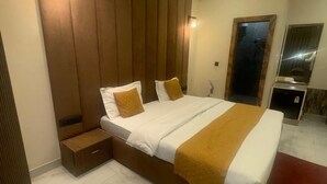 A modern hotel room with a large bed, a wooden accent wall, and a small bedside table. - Hotel Rajshree (Hisar)