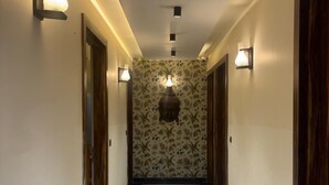 A hallway with a marble floor, wall-mounted lights, and a patterned wallpaper. - Hotel Rajshree (Hisar)