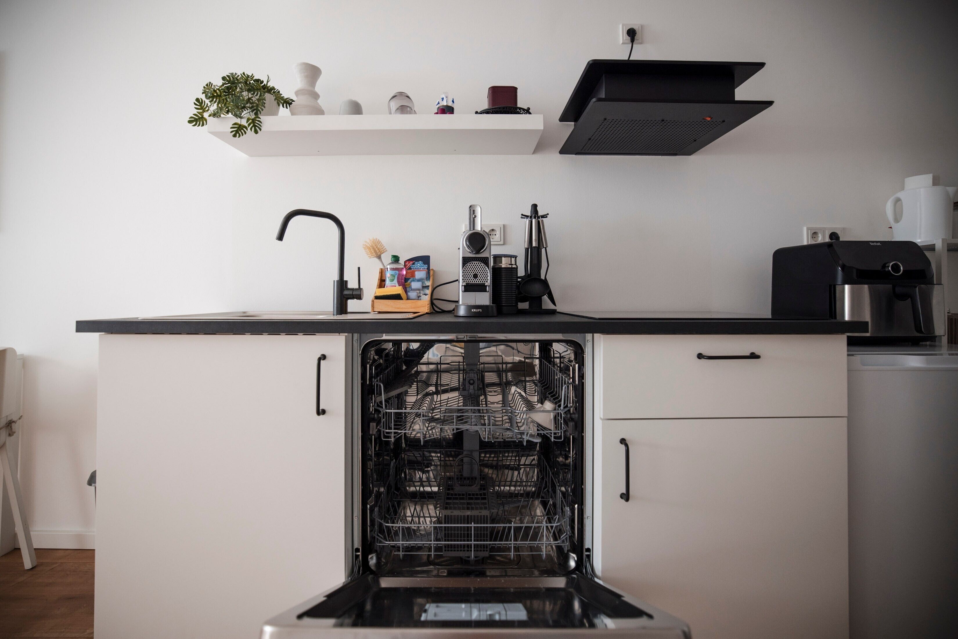 A kitchen with a dishwasher, a coffee machine, and a shelf with decorative items.