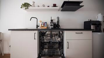 A kitchen with a dishwasher, a coffee machine, and a shelf with decorative items.