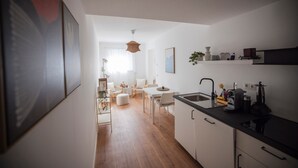 A modern kitchen with white cabinetry, a black countertop, and a dining area with a white table and chairs. - Luxury Apartment on the Edge of the Forest, Close to the City (Bornheim)