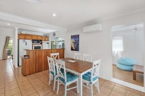 A modern kitchen with wooden cabinets, a microwave, and a refrigerator. There is a dining area with a wooden table and white chairs.