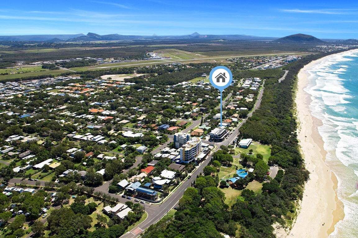 An aerial view of a coastal town with residential areas, a beach, and a prominent hotel icon indicating a hotel presence.