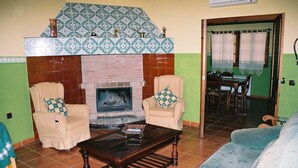 Ein Wohnzimmer mit Kamin, zwei Sesseln, einer Couch und einem Essbereich mit Tisch und Stühlen.