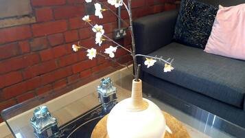 Una mesa de vidrio con un florero de flores blancas, un objeto metálico decorativo y un cojín en un sofá.