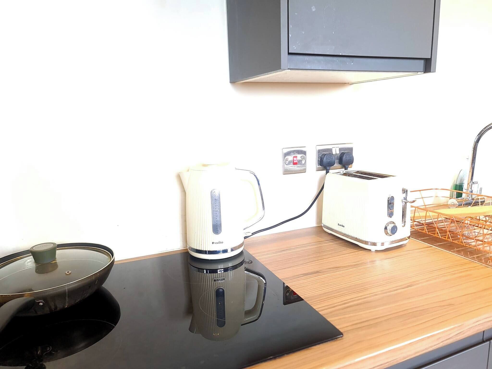 A kitchen with a stovetop, a kettle, a toaster, and a sink.