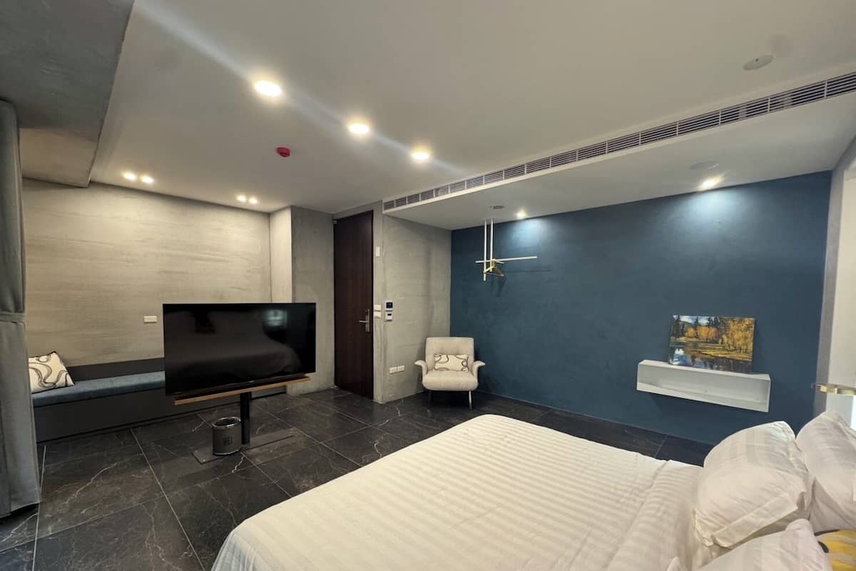 A modern bedroom with a large bed, a TV, a chair, and a painting on the wall.