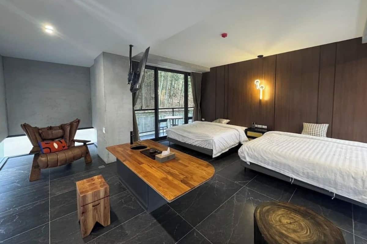A modern bedroom with two beds, a wooden coffee table, a small stool, and a chair with a cushion.