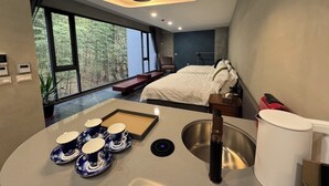 Quarto moderno com uma cama grande, uma mesinha de cabeceira e uma janela com vista para uma floresta.