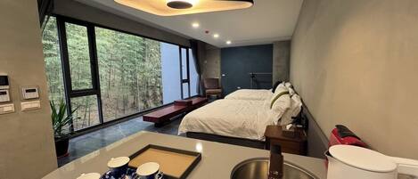 A modern bedroom with a large bed, a bedside table, and a window with a forest view.
