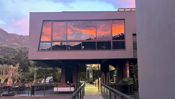 Um edifício moderno com fachada de vidro, uma cobertura e vista para a paisagem ao redor.