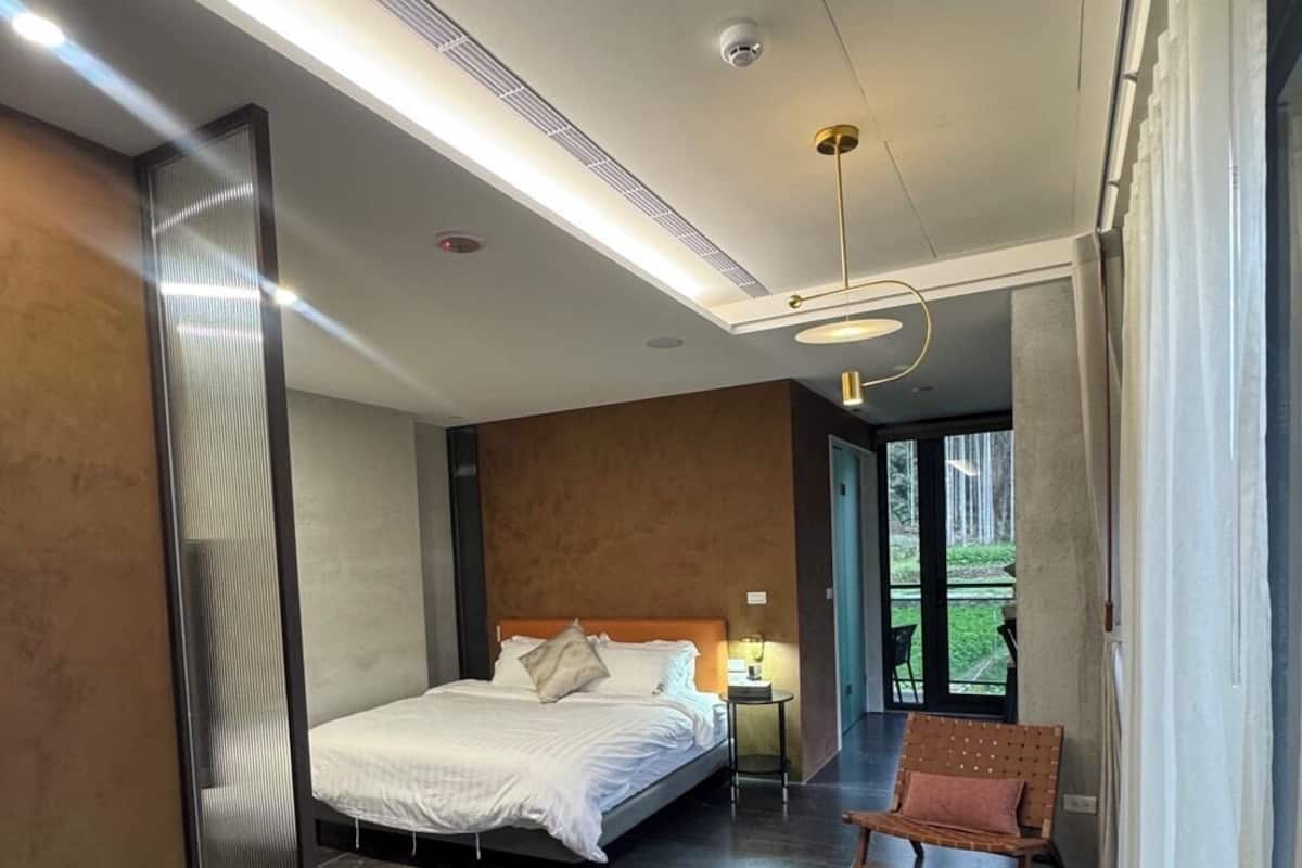 A modern bedroom with a large bed, a bedside table, a chair, and a view of the outdoors.