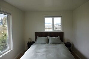 A bedroom with a bed, two bedside tables, a window, and a view of the outside.
