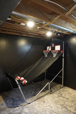 A basketball hoop with a net and two basketballs, a metal structure, and a ceiling with exposed beams and wiring.