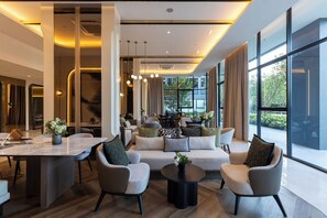 A modern hotel lobby with a central seating area, a dining space, and large windows offering views. - The Hampton Suites Bangna (Bangkok)