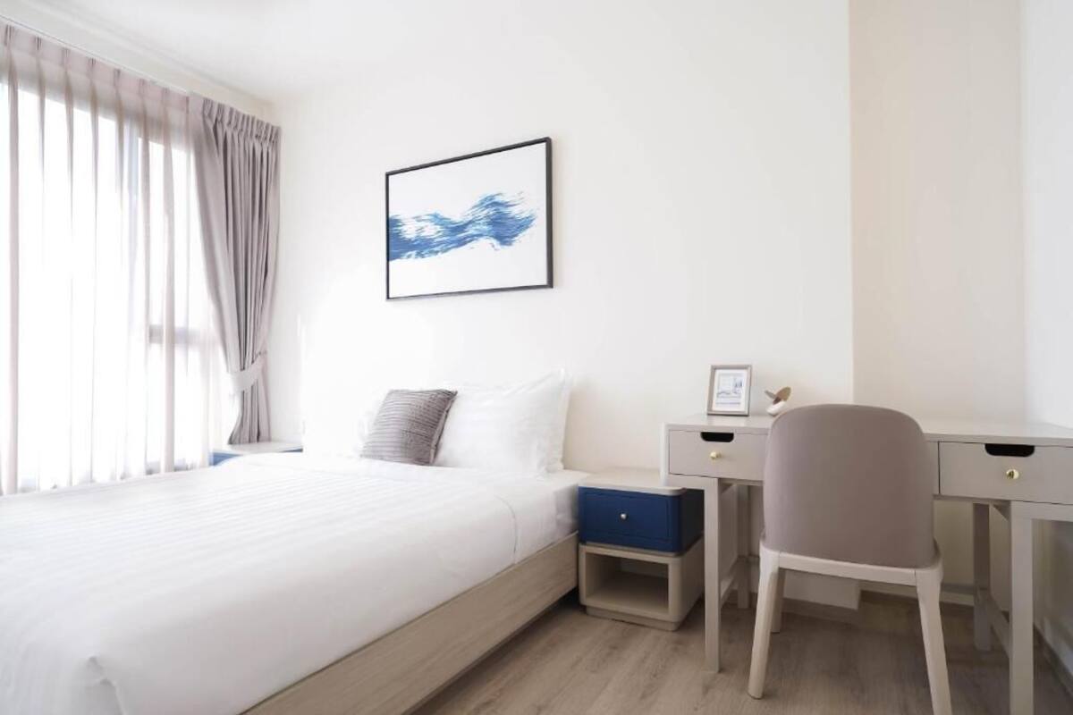 A hotel room with a bed, a desk, a chair, a nightstand, and a framed picture on the wall.