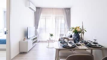 A modern living room with a dining area, a flat-screen TV, and a dining table set for two with a vase of flowers.