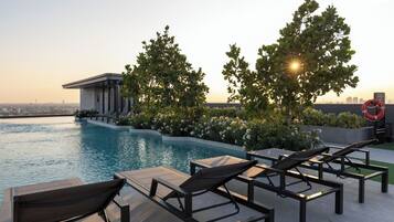 A rooftop pool with lounge chairs, a lifebuoy, and a view of the city skyline.