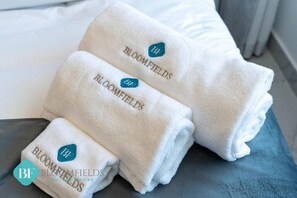 Three neatly folded white towels with the text "BLOOMFIELDS" and a logo on them, placed on a grey surface. - Bloomfields New STU in Oasis Masdar  (Abu Dhabi)