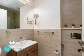A modern bathroom with a sink, mirror, towel rack, and shower area. - Bloomfields New STU in Oasis Masdar  (Abu Dhabi)