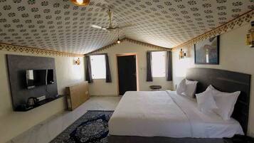 Een slaapkamer met een groot bed, een flatscreen televisie aan de muur, een plafondventilator en een kamerkleed met een patroon.