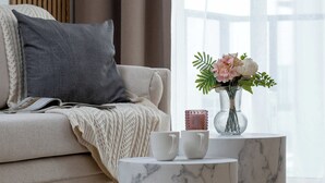 Ett vardagsrum med en soffa, en vas med blommor och två sidobord i marmor.