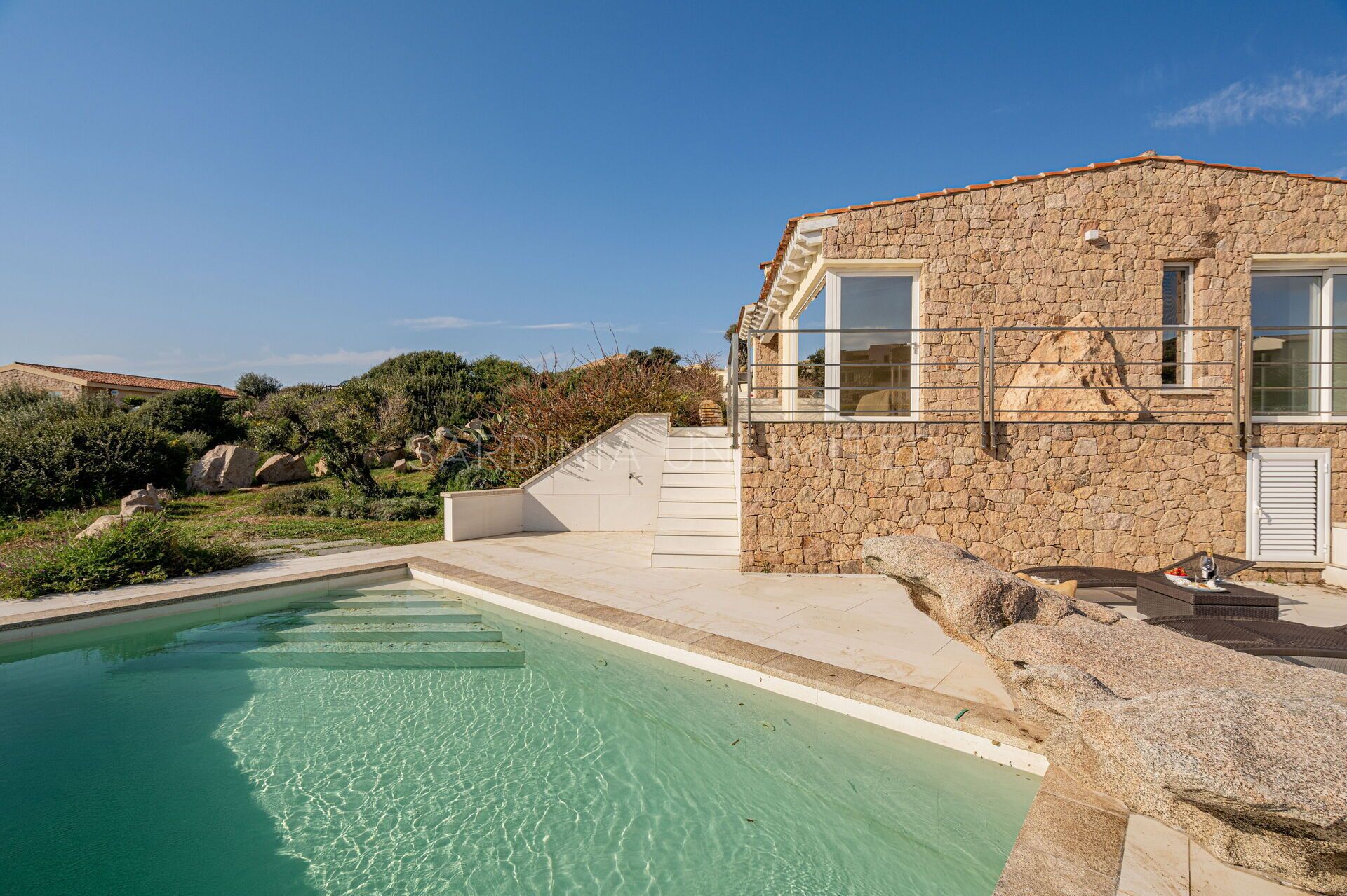 A stone building with a pool, steps leading to a terrace, and a clear blue sky.