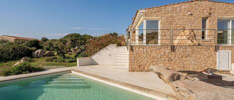 A stone building with a pool, steps leading to a terrace, and a clear blue sky.