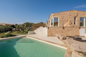 A stone building with a pool, steps leading to a terrace, and a clear blue sky.