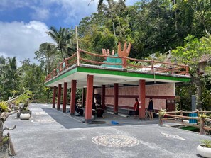 A building with a green roof and a red railing, surrounded by lush greenery.