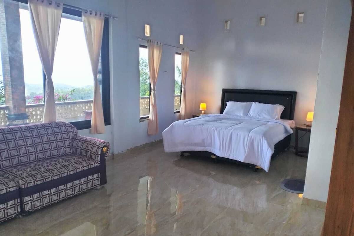 A bedroom with a bed, a sofa, and a balcony with curtains.