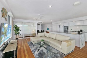 Uma sala de estar moderna com um sofá bege, uma mesa de centro de vidro e uma TV em um suporte de madeira.