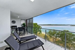 Varanda com vista para a praia e o mar. Há duas cadeiras de sol pretas e uma mesa com cadeiras.