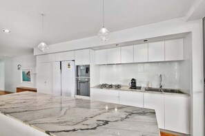 Uma cozinha moderna com armários brancos, uma ilha de mármore e iluminação pendente.