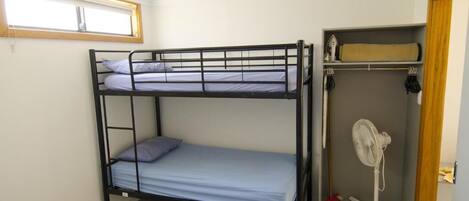 A bunk bed room with a window, a fan, and a storage shelf.