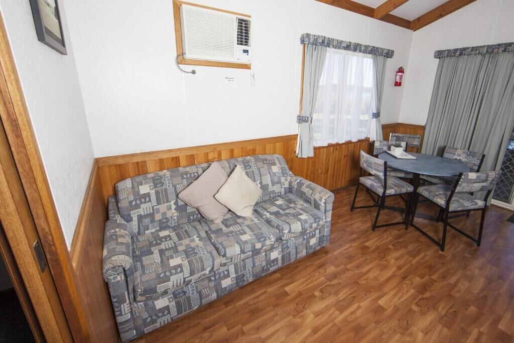 Et værelse med en stribet sofa, et spisebord med stole, et vindue med gardiner og en vægmonteret aircondition.
