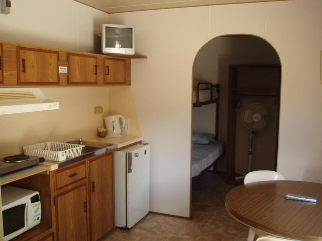 A compact kitchen with wooden cabinets, a microwave, a refrigerator, a small sink, and a television on a shelf.