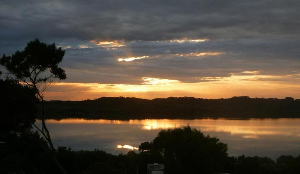Un capvespre sobre un llac tranquil, amb la silueta d'arbres i una riba llunyana.