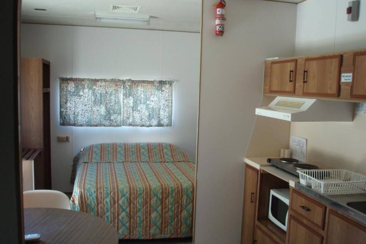 Une pièce de taille modeste comprenant un lit, une petite kitchenette, une fenêtre avec des rideaux et un extincteur.