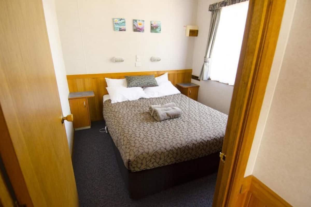Une chambre d’hôtel comprenant un lit, deux tables de chevet, une commode, une fenêtre avec des rideaux et des œuvres d’art accrochées au mur.