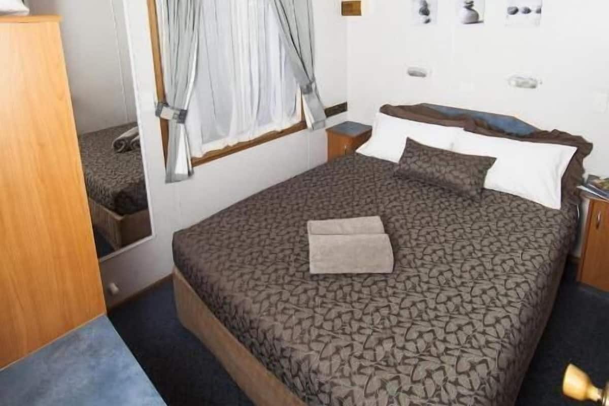Une chambre à coucher comprenant un lit, un ventilateur de plafond, une fenêtre avec des rideaux, une table de chevet et un miroir.