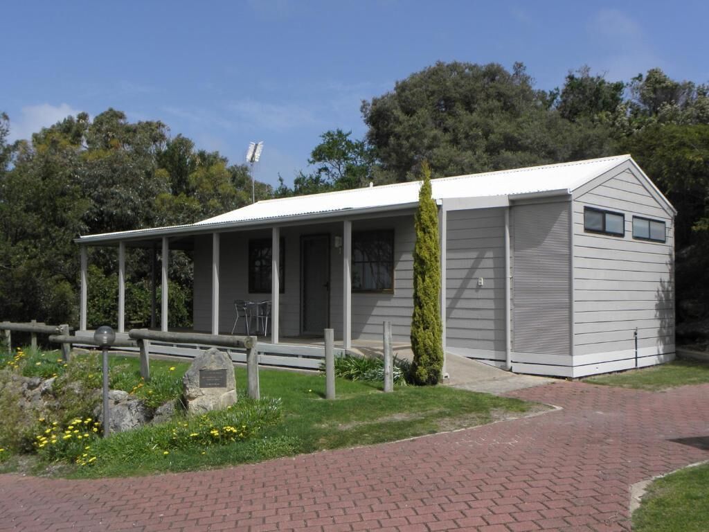 A single-story building with a covered porch, a small attached garage, and a landscaped garden with a pathway leading to the entrance.