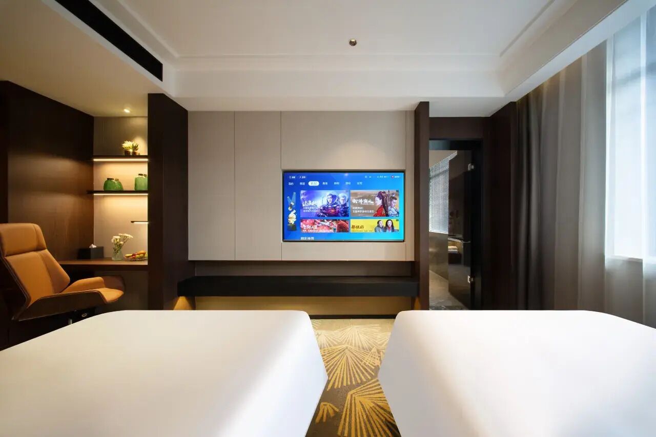 Une chambre d’hôtel équipée d’un téléviseur à écran plat fixé au mur, d’un canapé, d’un lit et d’une petite table agrémentée d’objets décoratifs.