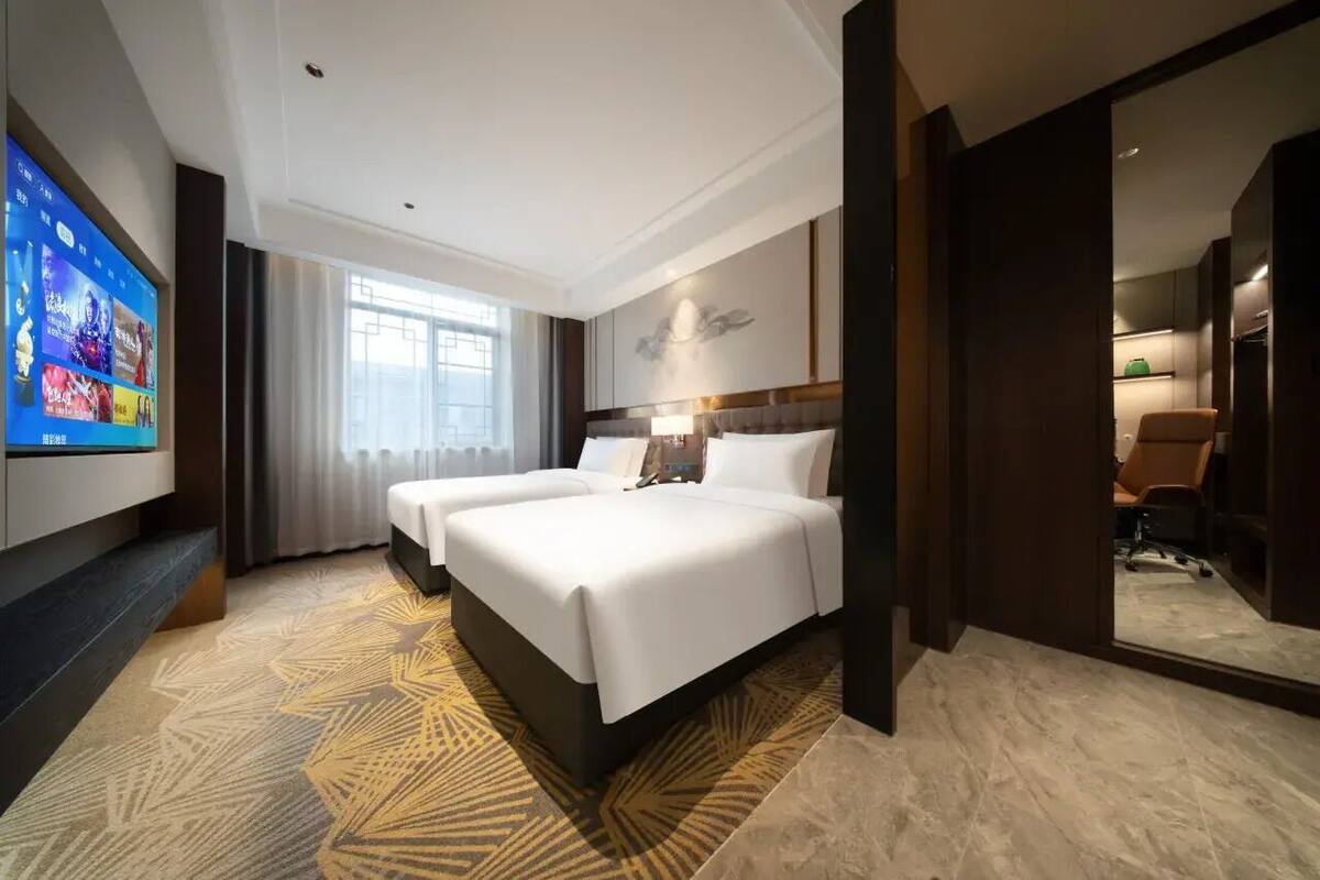 Ein Hotelzimmer mit einem großen Bett, einem an der Wand befestigten Fernseher und Blick auf die Stadt durch das Fenster.