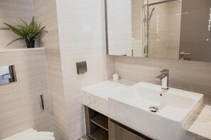 A modern bathroom with a large mirror, a white sink, and a potted plant. - Hampton Residence Thonglor (Bangkok)