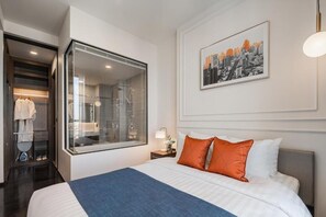 A hotel room with a large bed, a glass shower enclosure, a cityscape artwork on the wall, and a neatly organized closet. - Hampton Residence Thonglor (Bangkok)