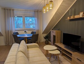 A modern living room with a sofa, dining table, chairs, TV, and decorative lights. - Stylish vacation apartment to feel good - central and quiet (Chemnitz)