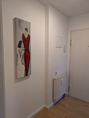 Een gang met een schilderij van twee vrouwen, een radiator en een deur.