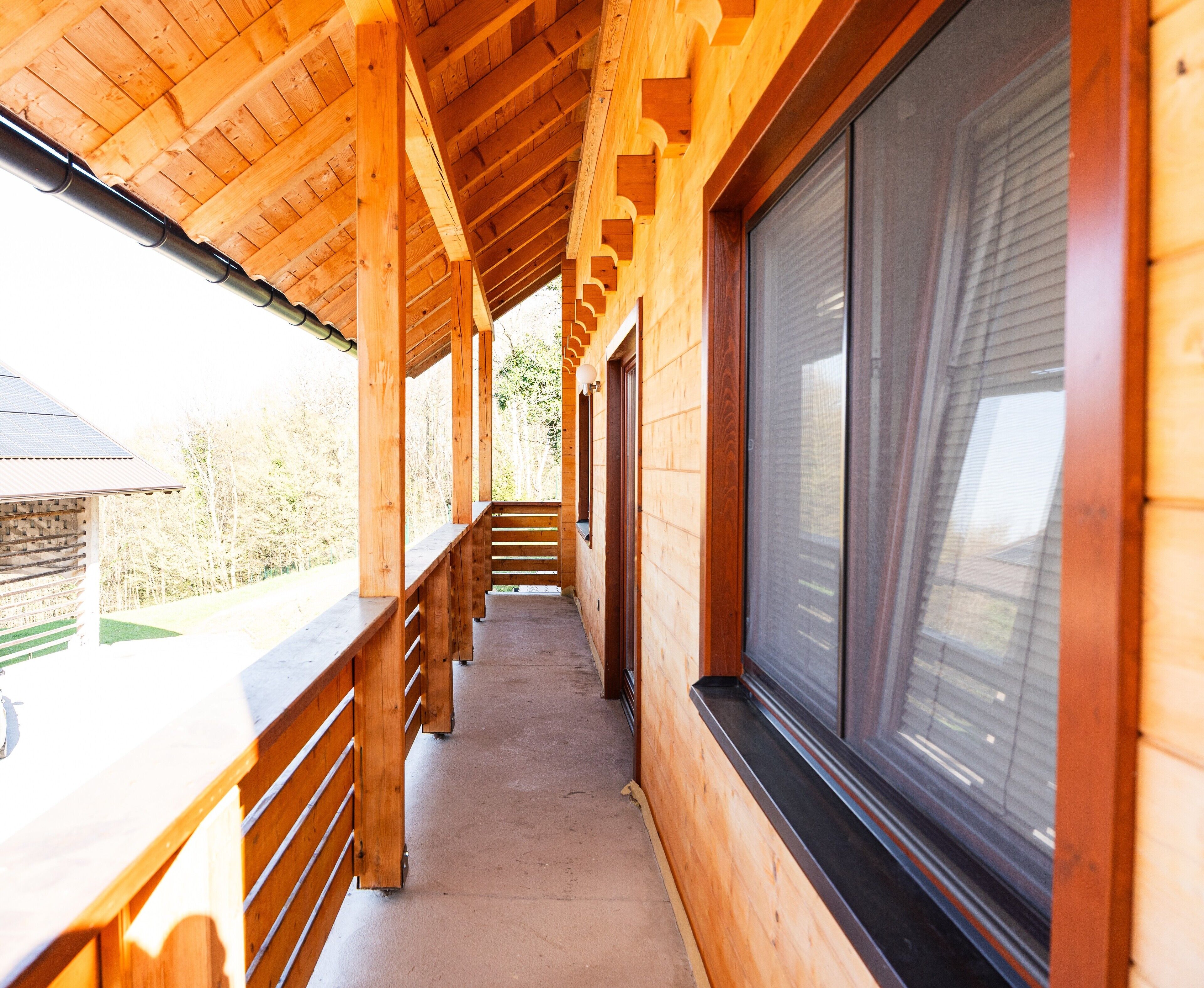 A wooden corridor with benches, large windows, and a view of the outdoors.